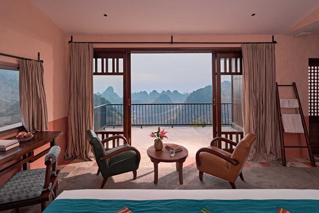 Chambre de bungalow au Ha Giang Aya Lodge avec une grande fenêtre et un balcon donnant sur les montagnes du plateau karstique de Dong Van.