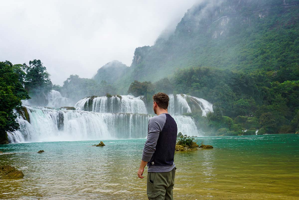 man standing in front of the Ban Gioc Waterfall in Cao Bang province