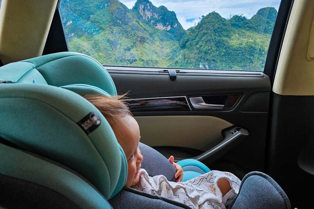 Ha Giang with baby, with baby sitting in a baby car seat in a car while driving along the Ha Giang Loop