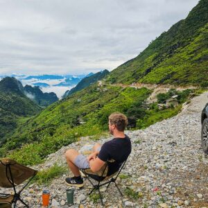 Ha Giang Loop By car with man sitting next to a car and Ha Giang's mountains as backdrop