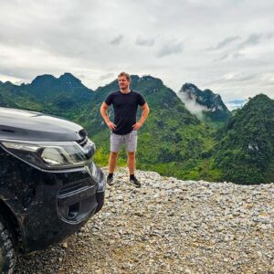 Ha Giang Loop by car, man standing next to car with views over the mountains of Ha Giang